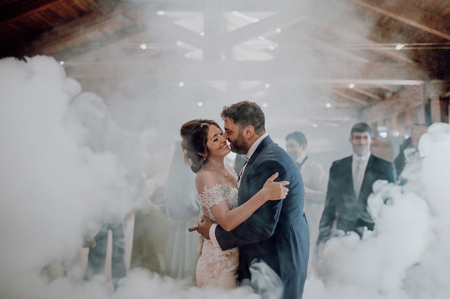 Bride and groom sharing first dance surrounded by dramatic white smoke clouds in rustic barn venue.