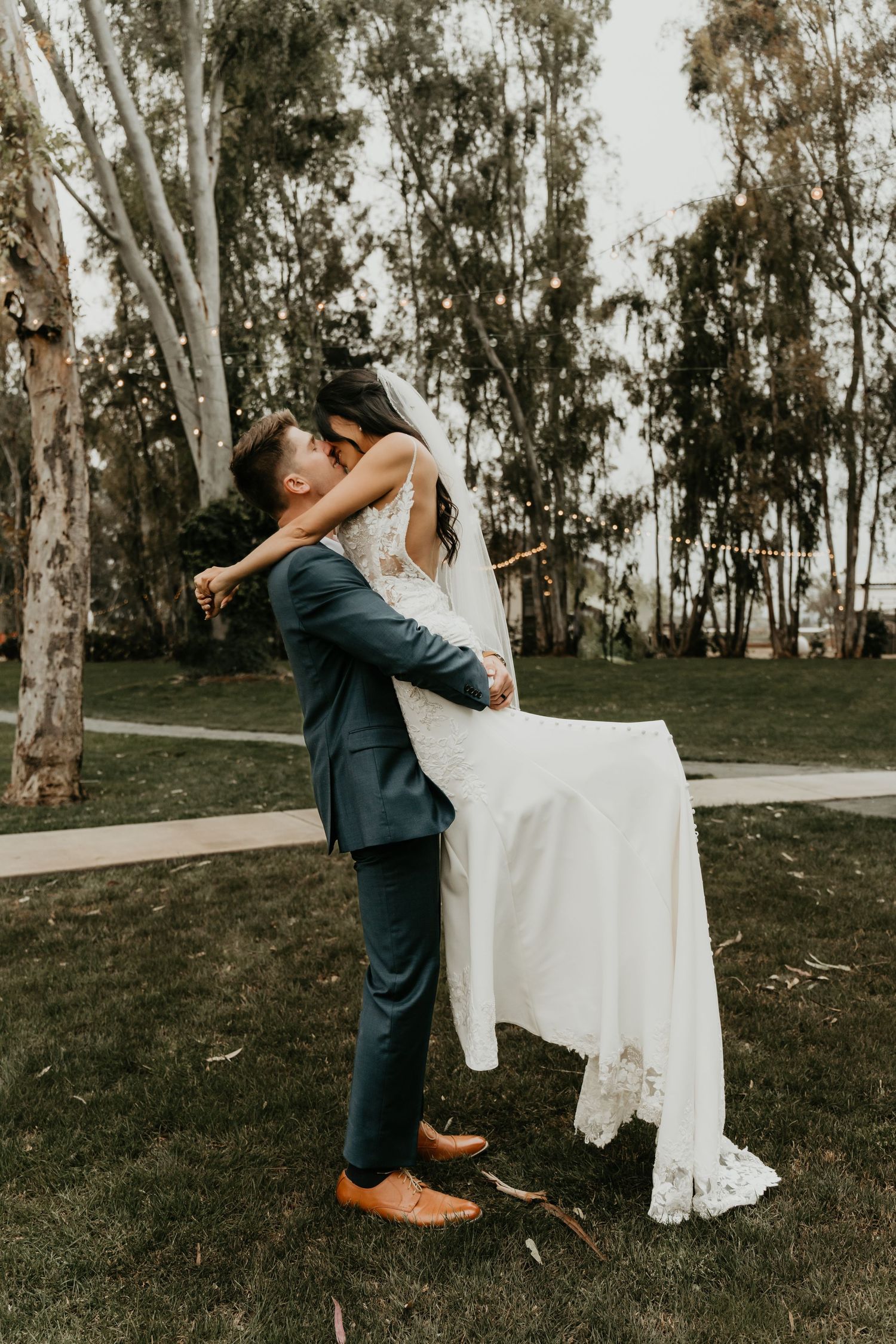 Romantic wedding couple embracing amongst eucalyptus trees in outdoor setting.