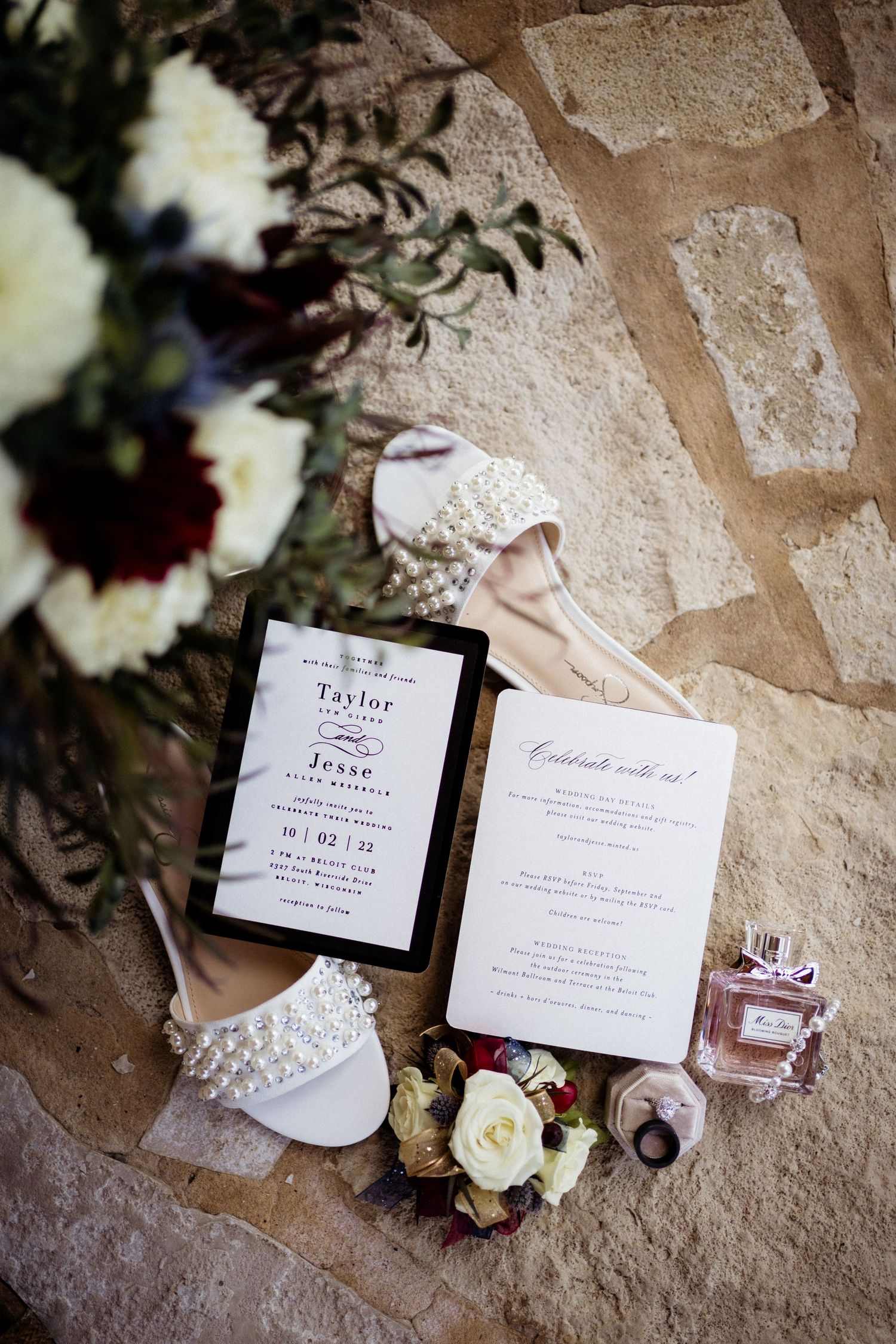 Wedding invitation suite with floral details, perfume bottle and bridal accessories on stone surface.