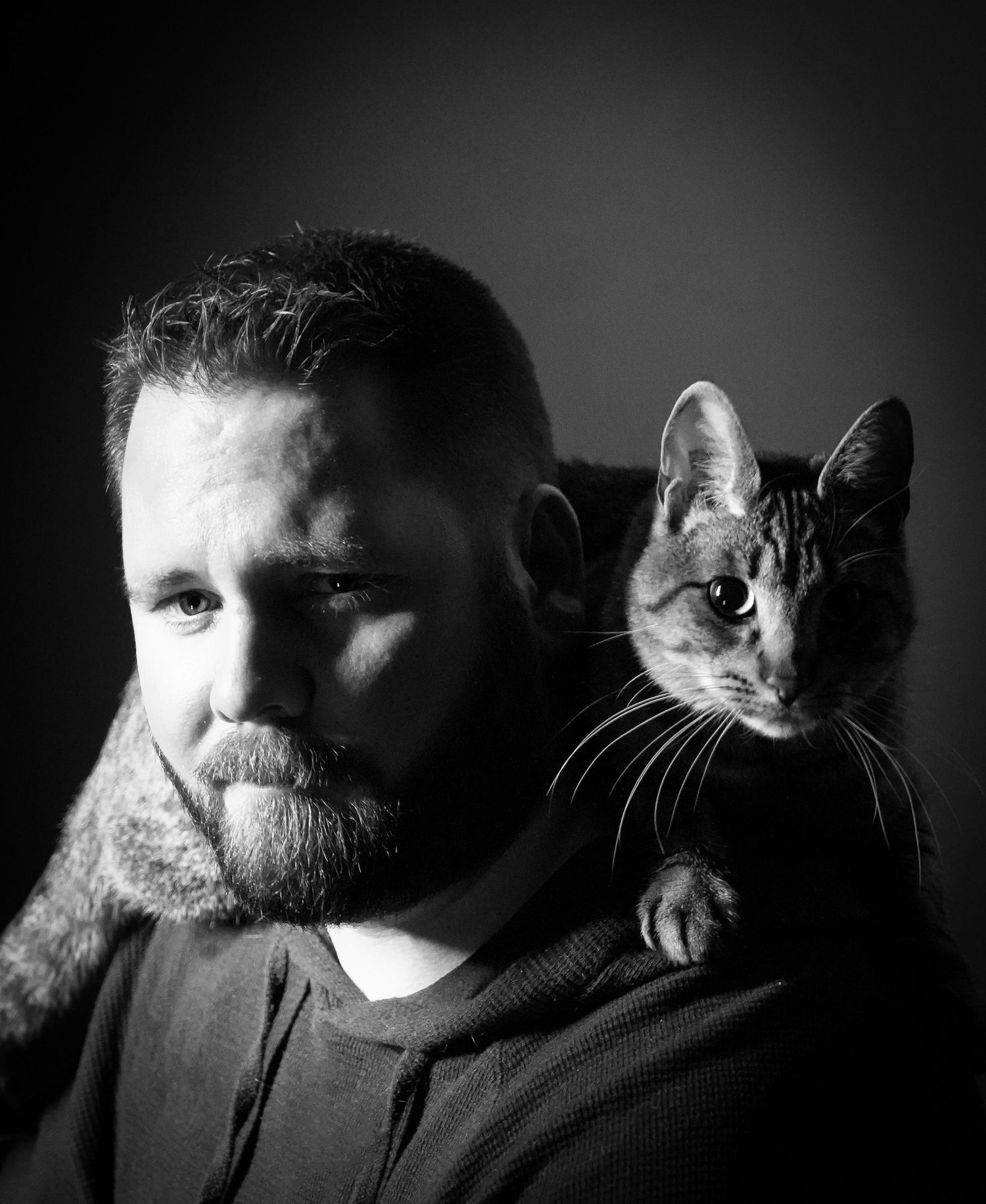 Striking monochrome portrait showing a cat resting comfortably on someone's shoulder.