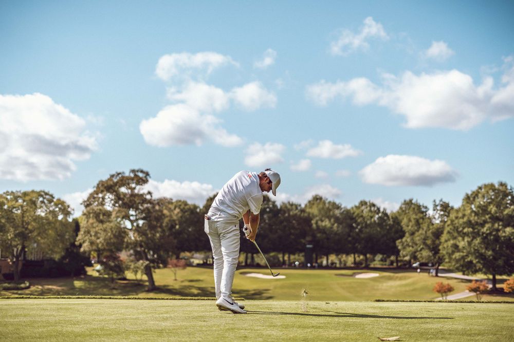 Golfer in white outfit completing swing motion on sunny golf course.