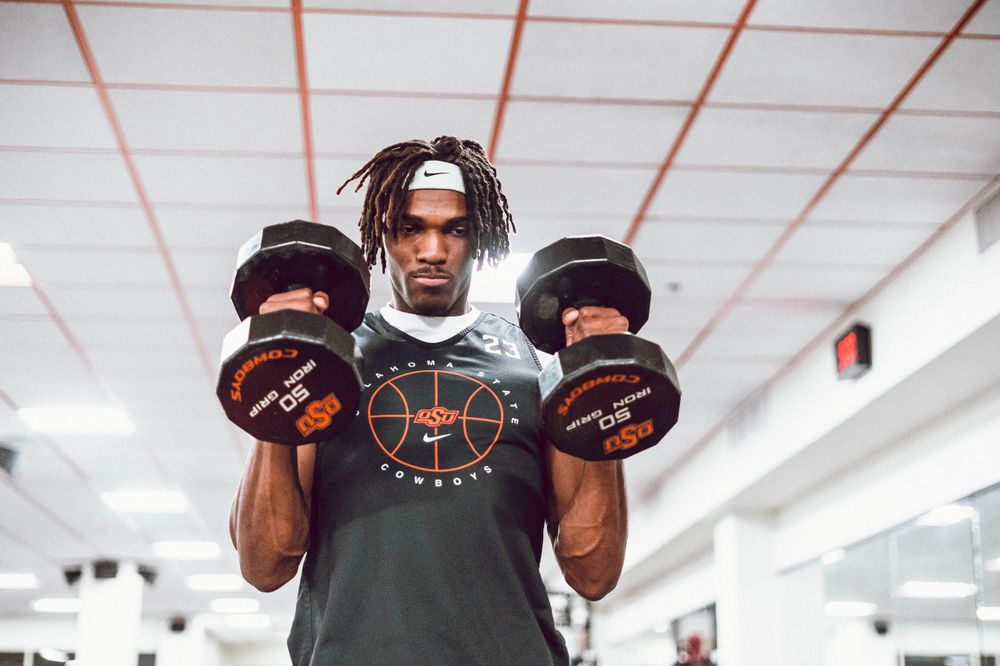 Person lifting dumbbells during workout session in bright indoor gym setting.