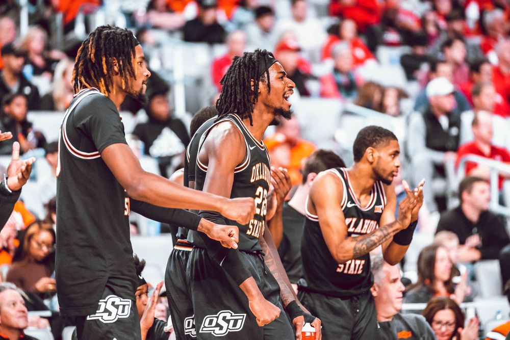 Oklahoma State basketball players standing together on sideline during game.