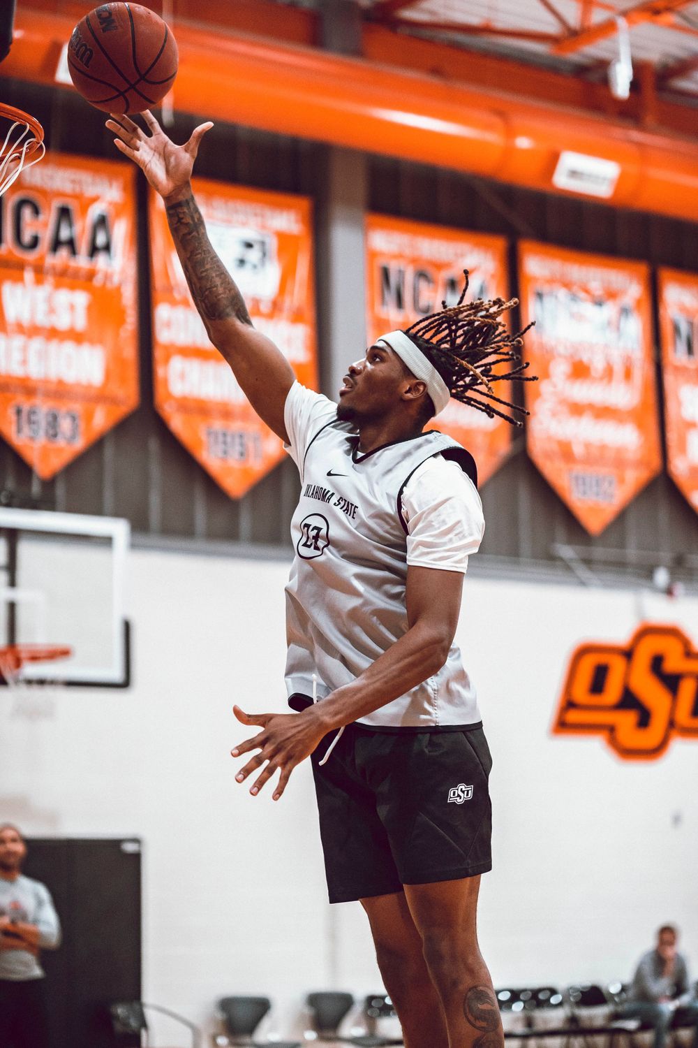 Player reaching up to catch basketball during practice with NCAA banners visible.