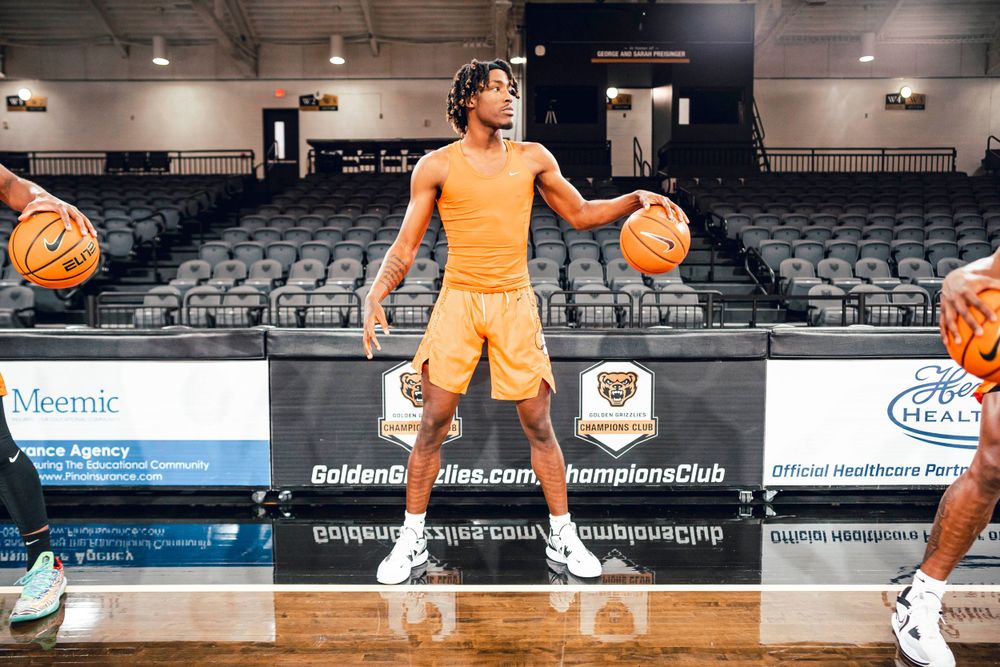 Basketball player in orange uniform holds multiple basketballs during practice drill.