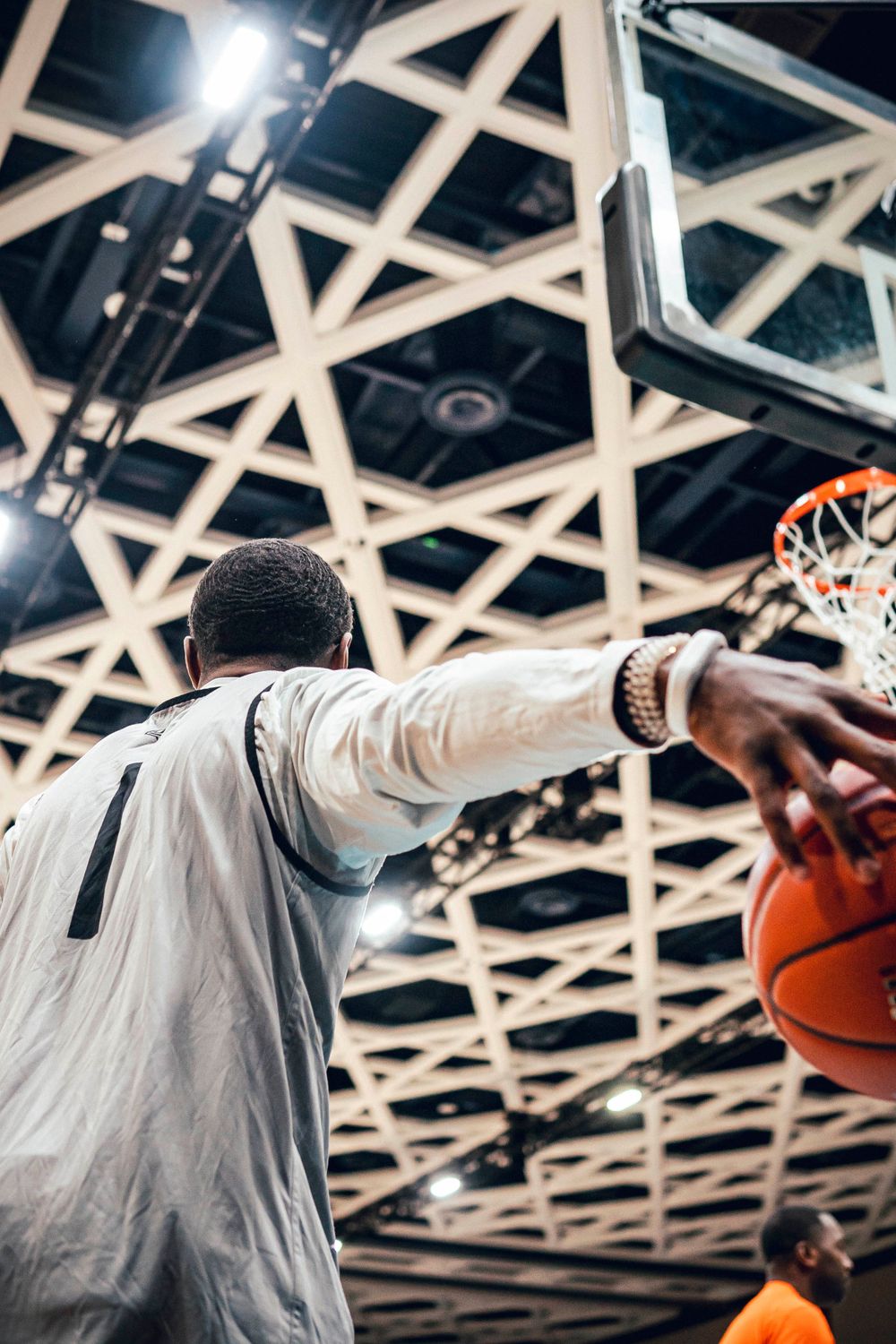 Basketball player extends arm toward hoop against geometric ceiling background.