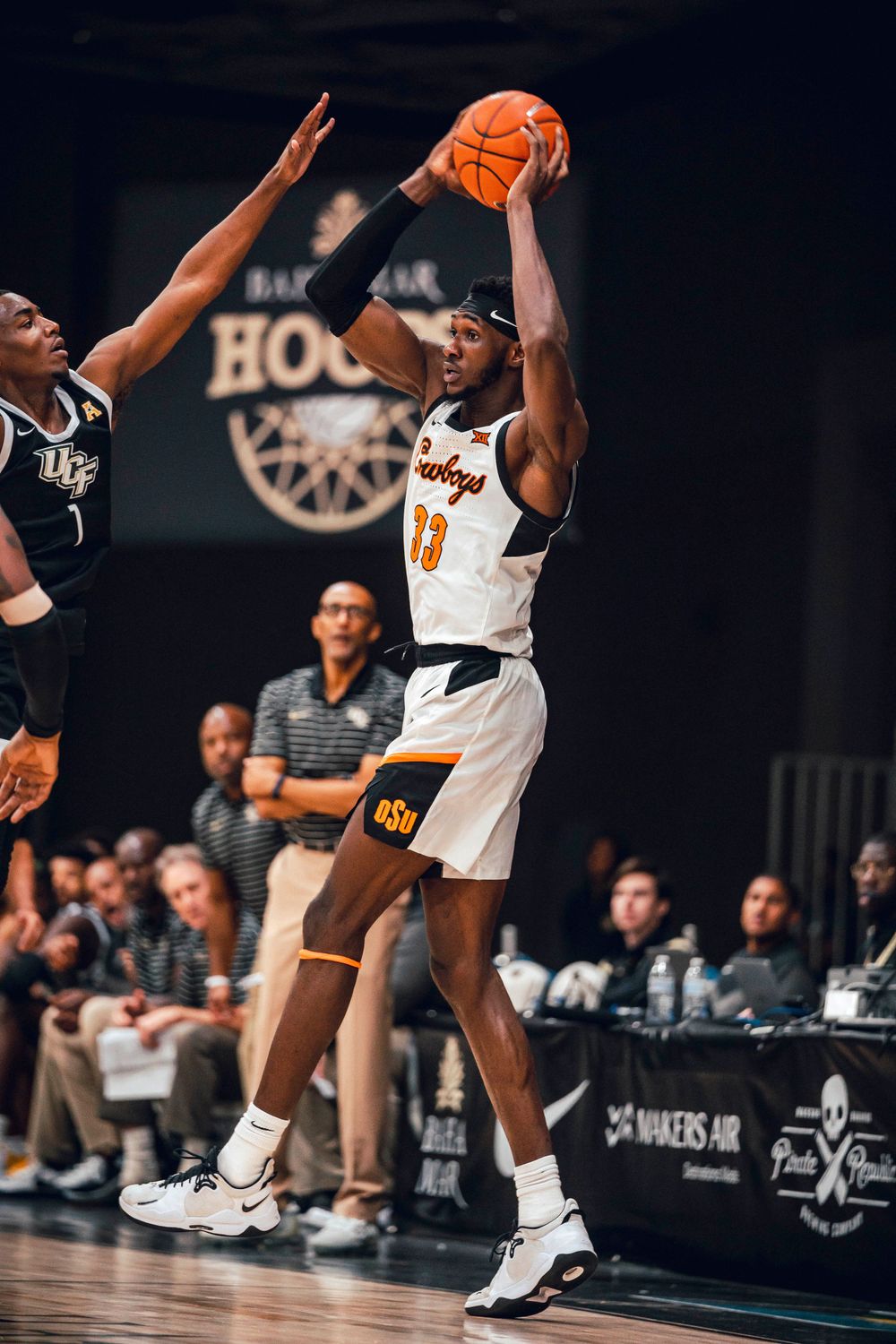 Basketball player in white jersey takes a shot while defender attempts to block.
