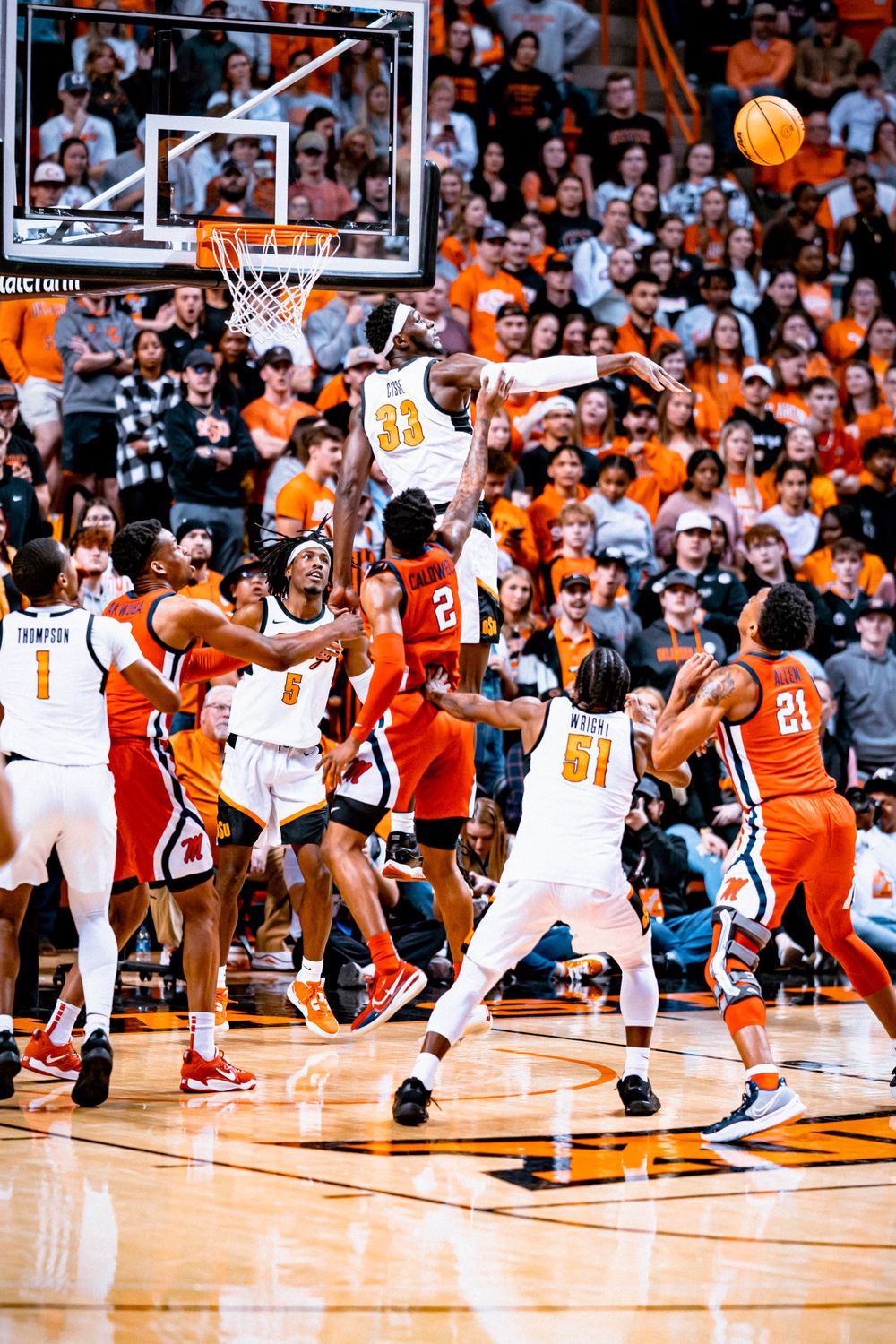 Basketball player leaps high above others during dramatic game action at college arena.