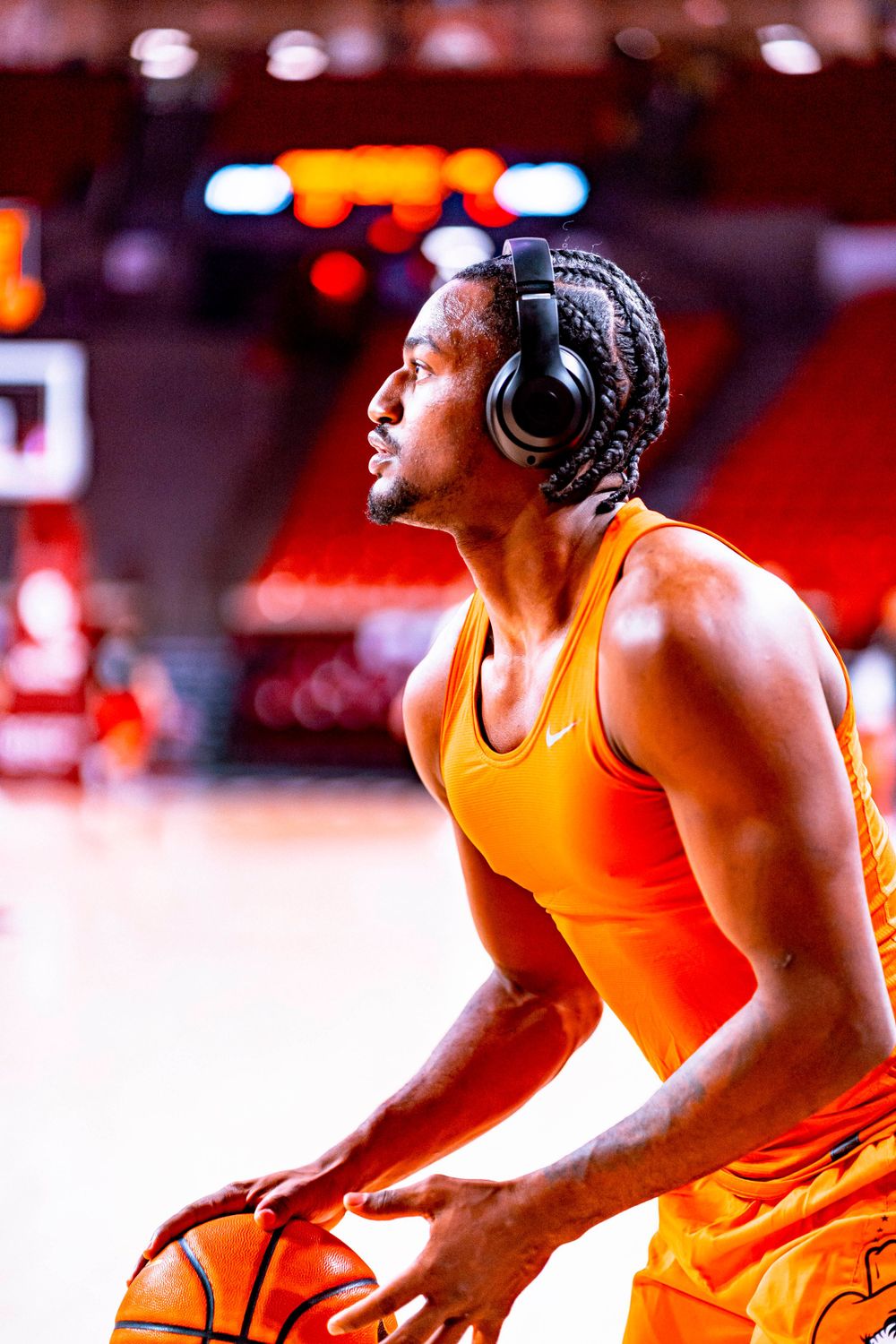 Basketball player in orange jersey wearing headphones prepares to shoot during pregame warmup.