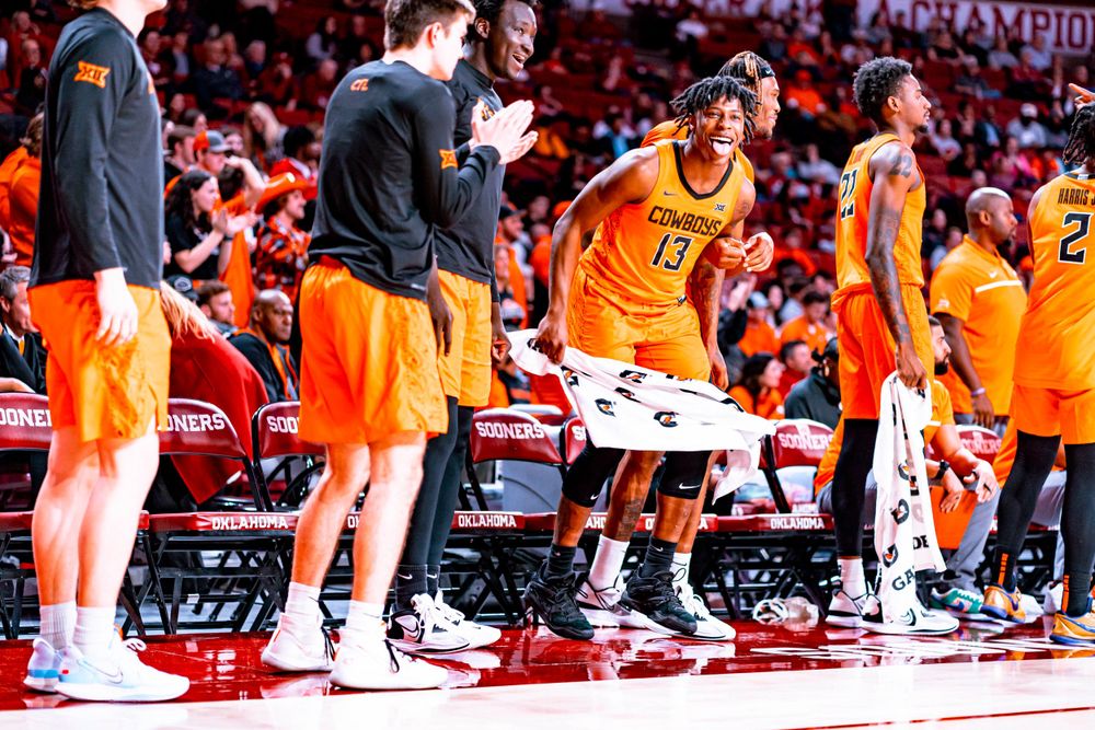 Oklahoma State basketball team members interact on sideline during game.