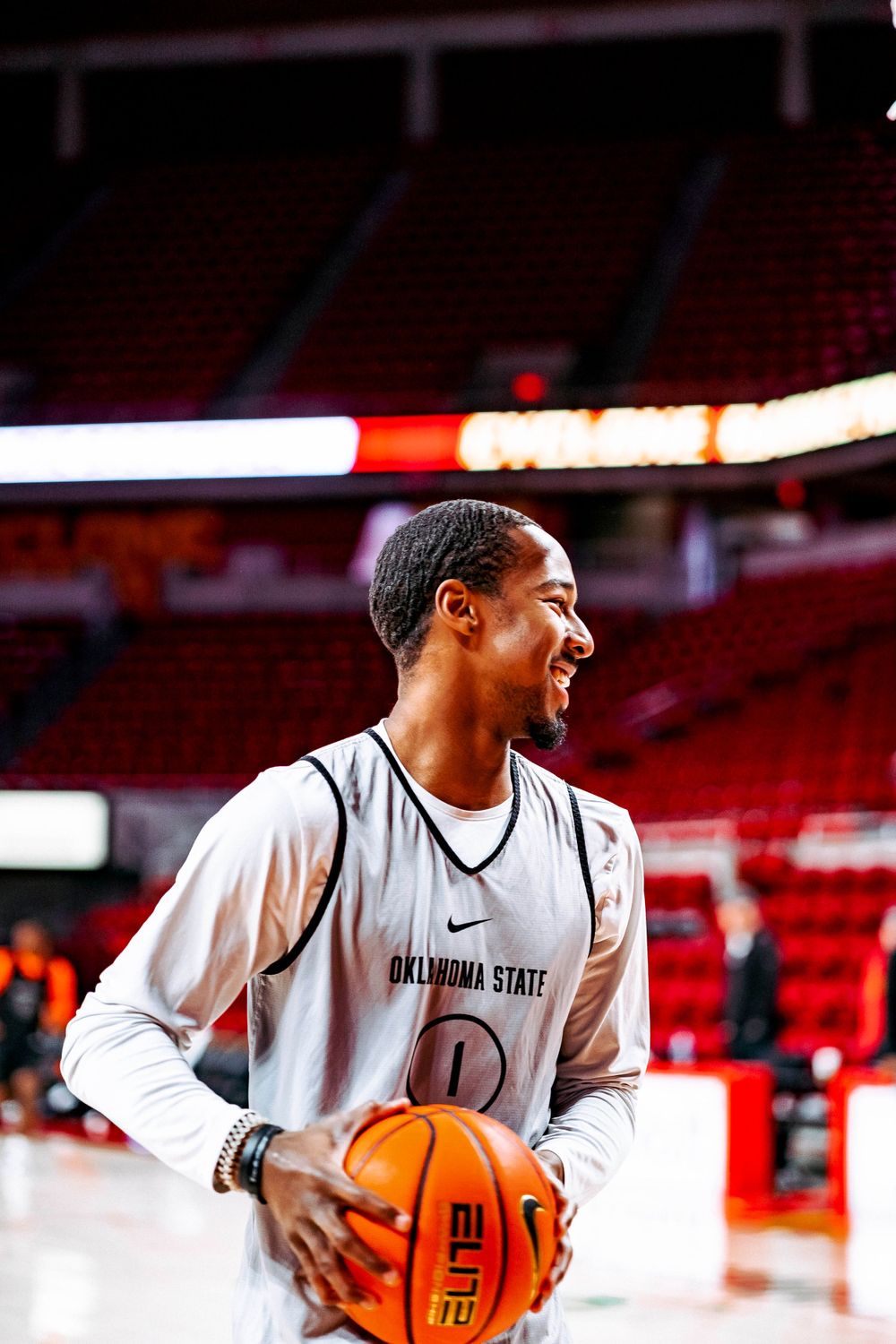 Basketball player in white Oklahoma State practice jersey holds ball while smiling.