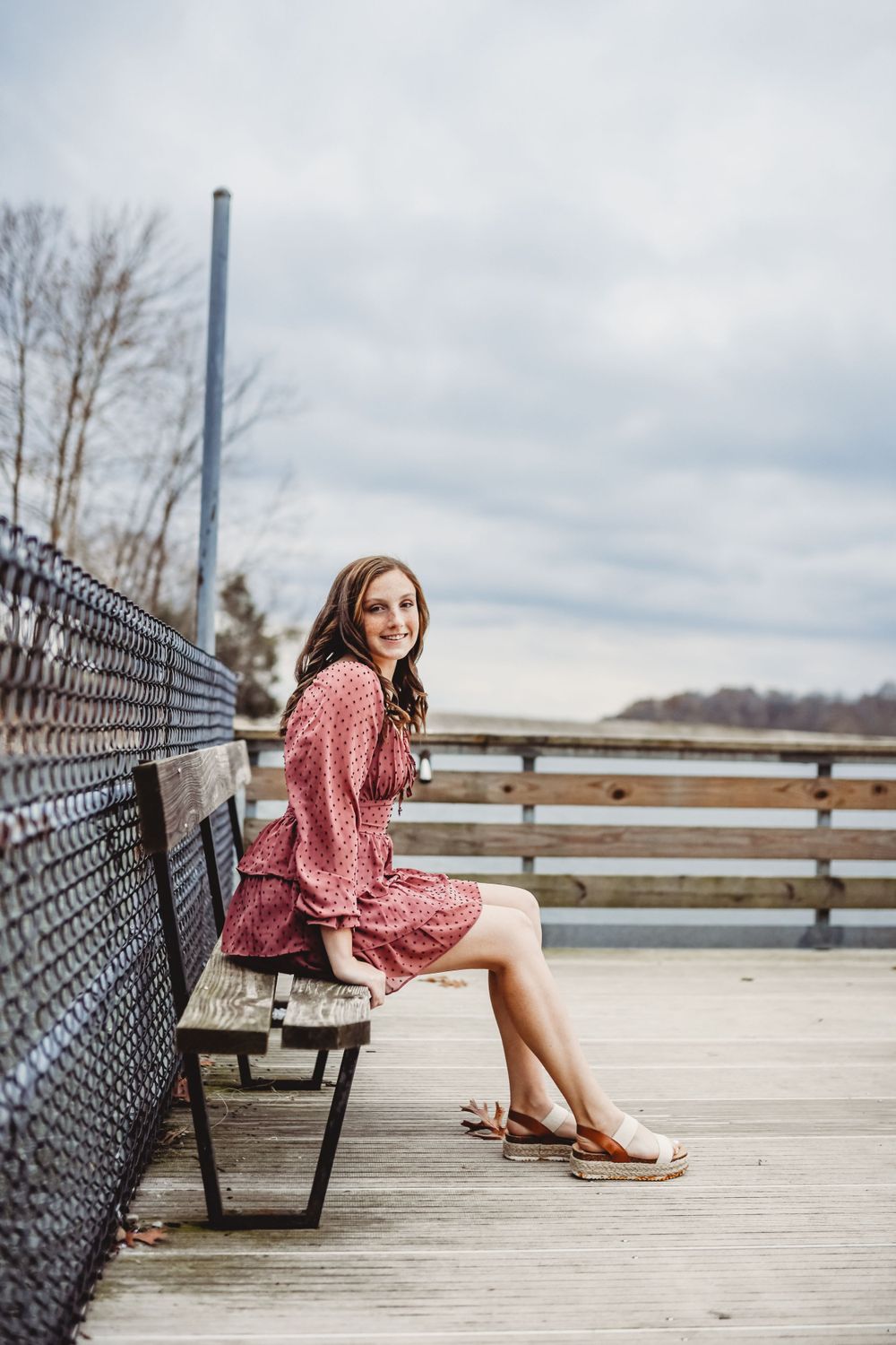 Portrait session on wooden deck with chain-link fence and cloudy sky backdrop.