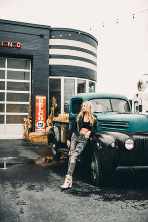 Urban fashion shoot with vintage car and industrial building backdrop.