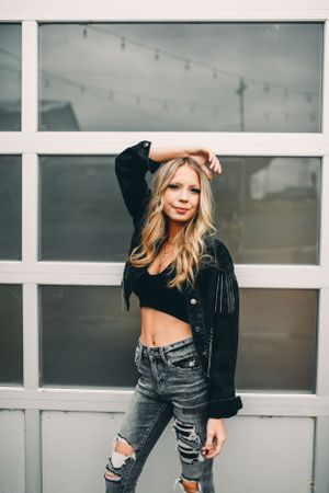 Fashion portrait against white windows featuring distressed jeans and black crop top.