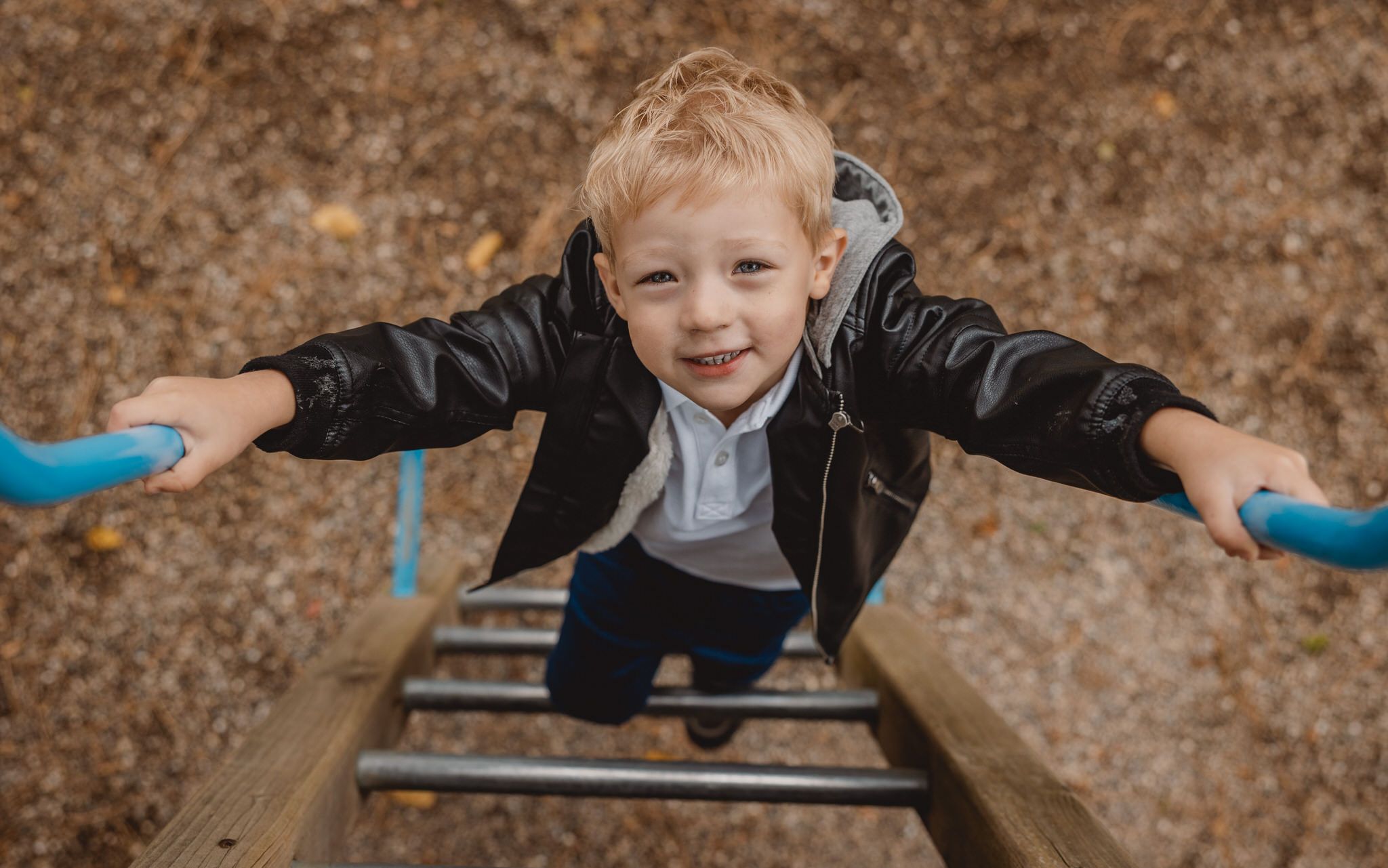 Candid photography of child playing on wooden rails in natural setting.