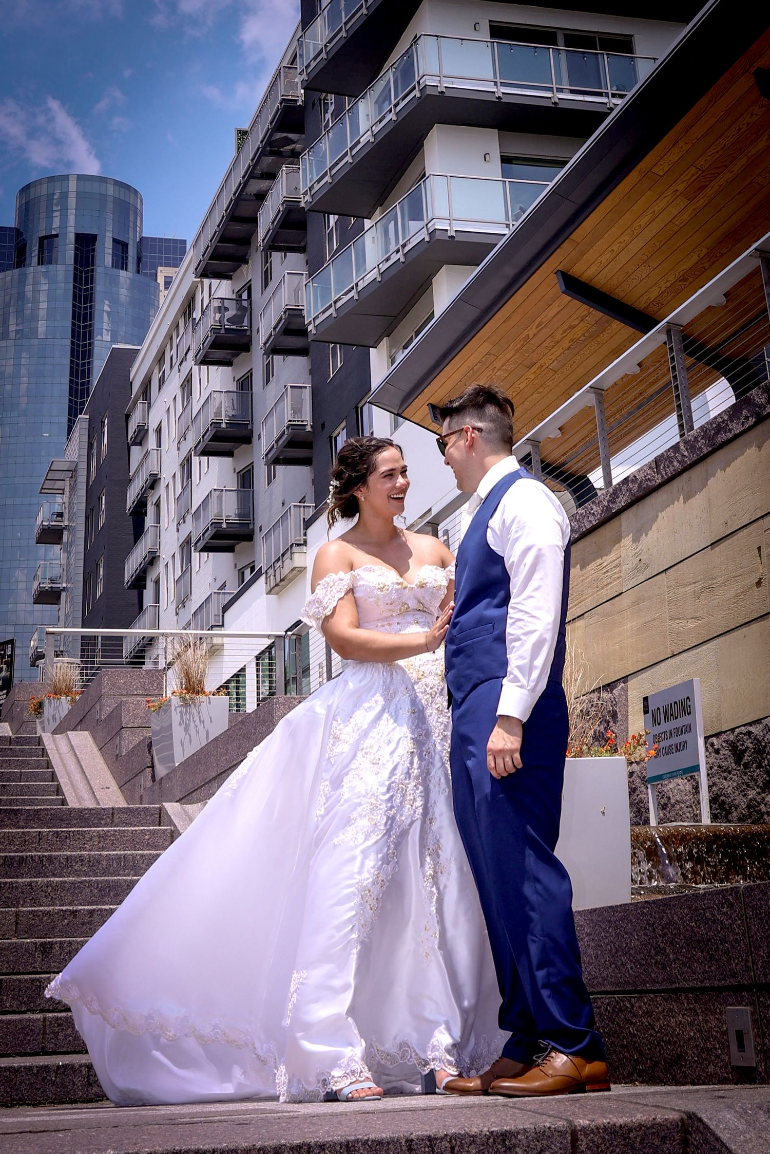 A newlywed couple poses on urban steps with a modern apartment building backdrop.