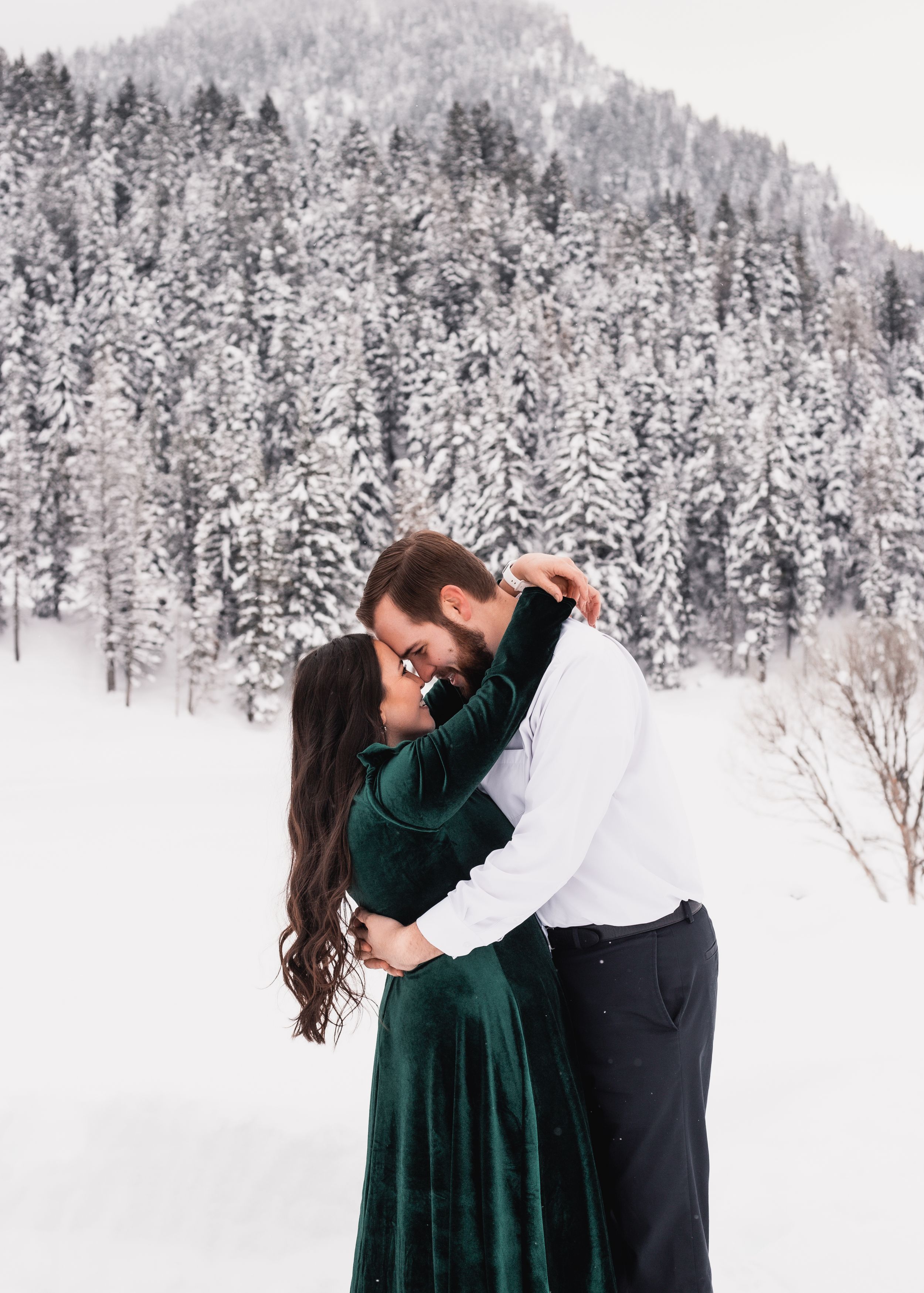 Romantic winter engagement photos with couple in snowy forest landscape.