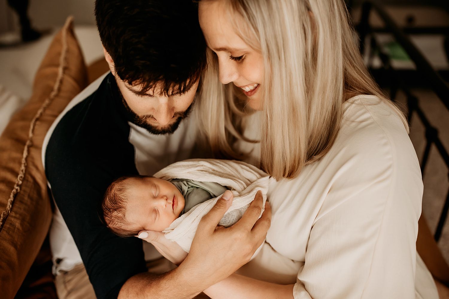 A mother and father hold their newborn baby boy while smiling down at him.