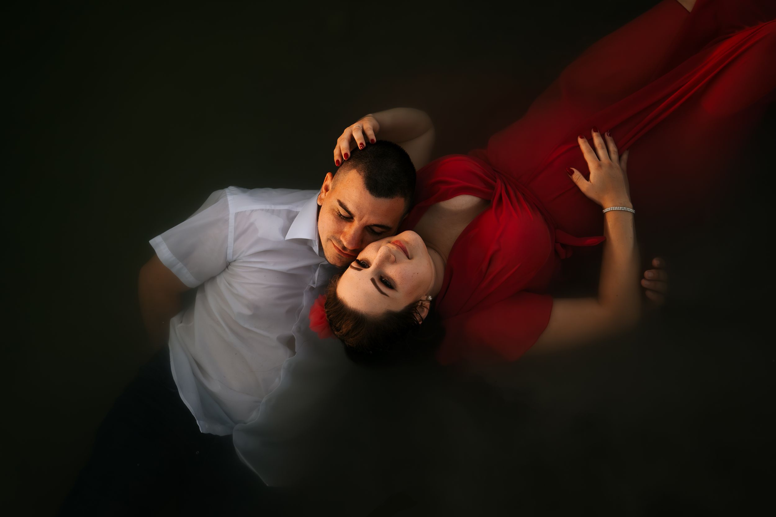 Artistic portrait of a couple in dramatic lighting against dark background.