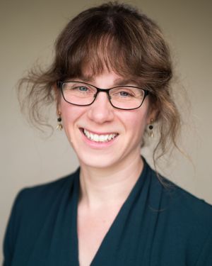 Professional portrait of someone wearing glasses and a dark teal blazer with a warm smile.