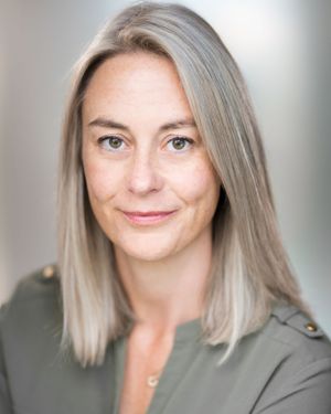 Professional headshot with shoulder-length platinum blonde hair wearing olive green top.