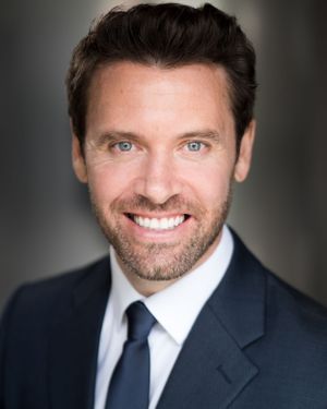 Business portrait of someone in a navy suit and tie with bright blue eyes and facial hair.