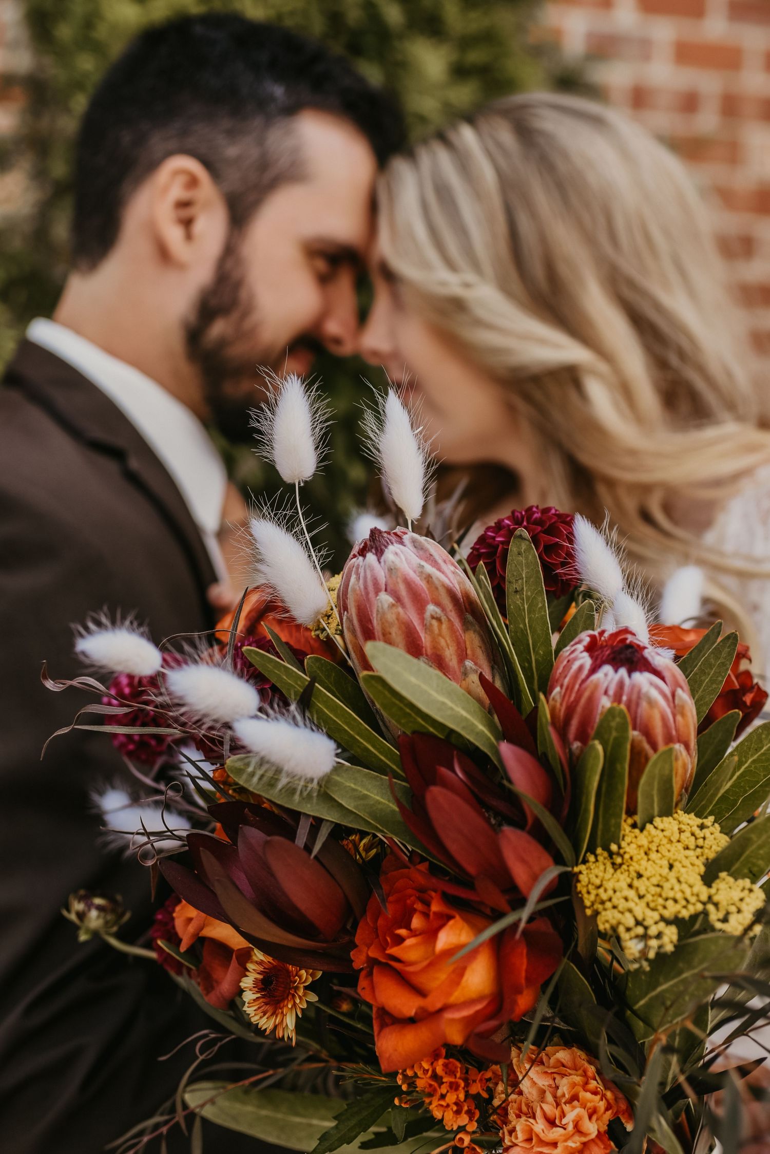 Vibrant autumn wedding bouquet with orange roses, protea, and white feather accents.