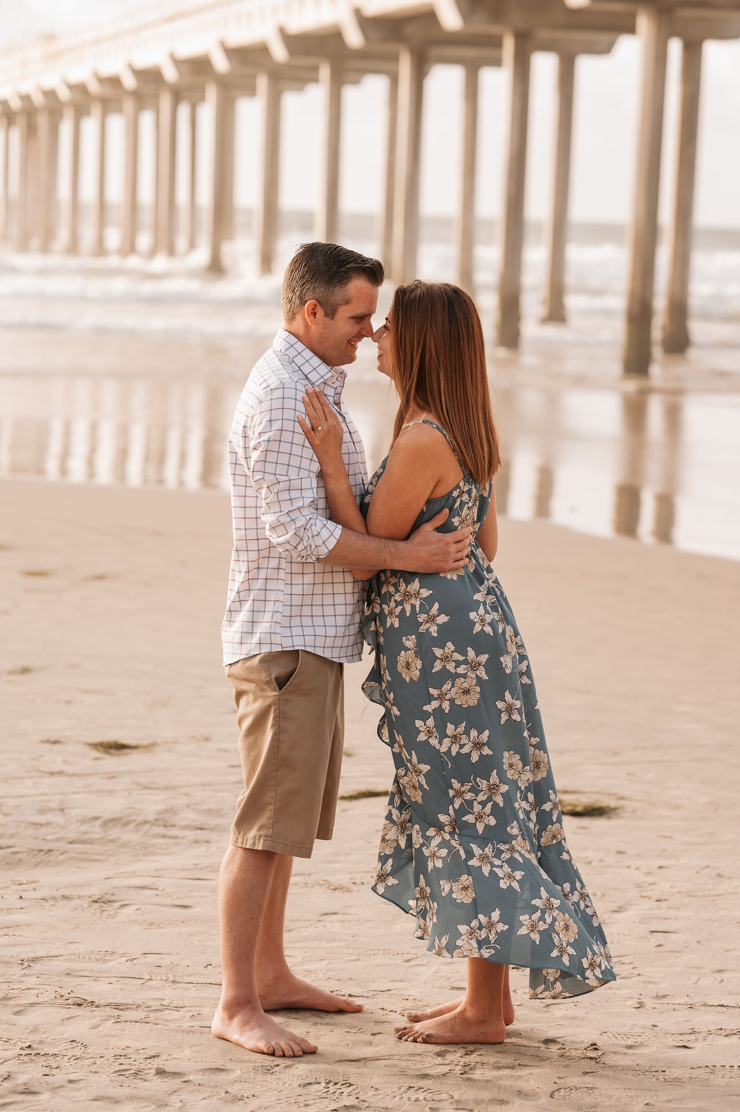 Romantic couple embracing on beach near pier during sunset.