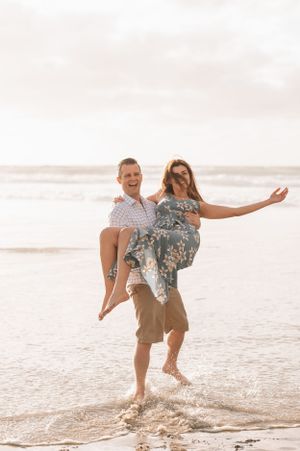 A playful couple shares a fun moment as he carries her while standing in the ocean surf.