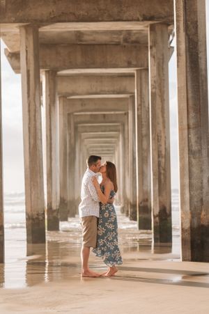 A couple shares an intimate moment beneath a pier's dramatic vanishing point architecture.