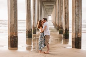 Romantic moment captured under a pier with geometric columns creating perspective to the horizon.