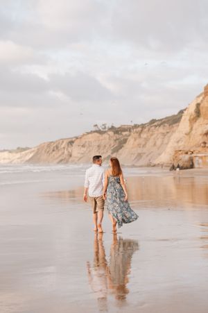 Beach scene with couple walking along shoreline near coastal cliffs at golden hour.