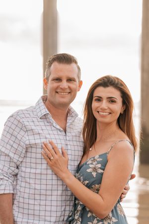 Engagement photo showing couple in casual attire under pier columns.