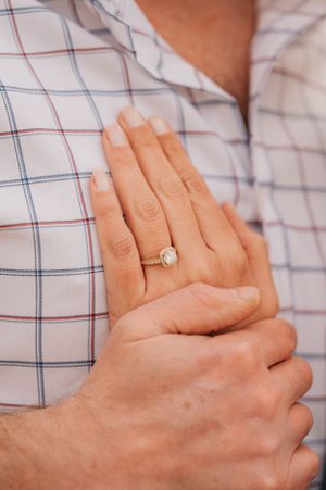 Close up of engagement ring on hand against checkered shirt background.