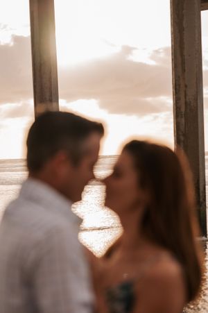 Silhouetted couple in romantic pose against sunset ocean backdrop.