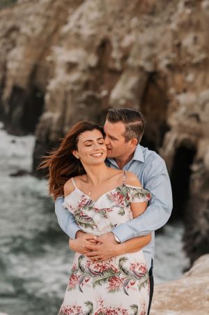 Intimate coastal portrait session showing tender embrace against dramatic ocean cliff backdrop.