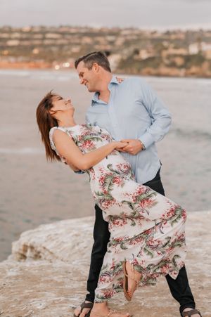 Playful dancing sequence of couple on beach rocks during sunset portrait session.