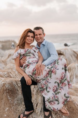Romantic coastal photoshoot featuring couple in intimate poses on rocky cliffside.