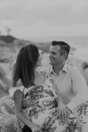 A romantic couple sitting together on a beach during a black and white photo session.
