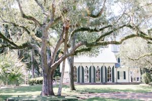A historic chapel with Gothic windows sits beneath sprawling oak trees covered in Spanish moss.
