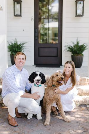 Couple sitting on front porch steps with their two dogs, a goldendoodle and black and white dog.