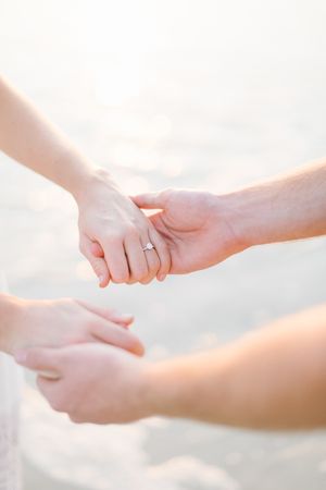 Close-up shot of hands holding with engagement ring in soft natural light.