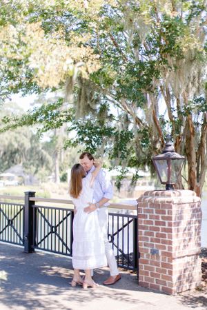 A couple shares a tender moment on a porch beneath Spanish moss draped trees.