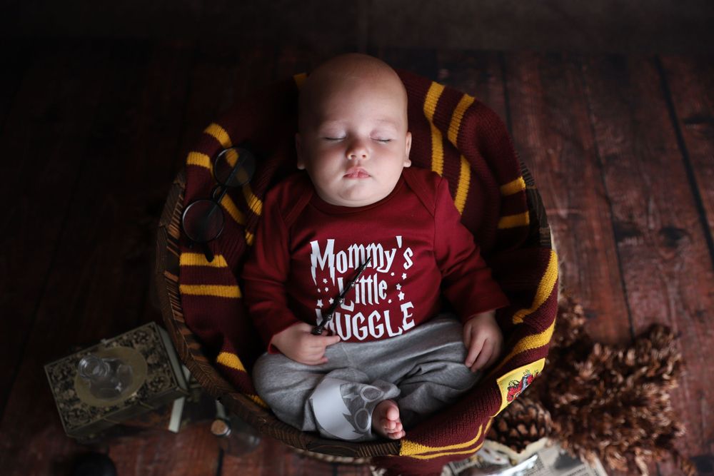 Newborn baby sleeps peacefully in Harry Potter themed Mommy's Little Muggle outfit in basket.