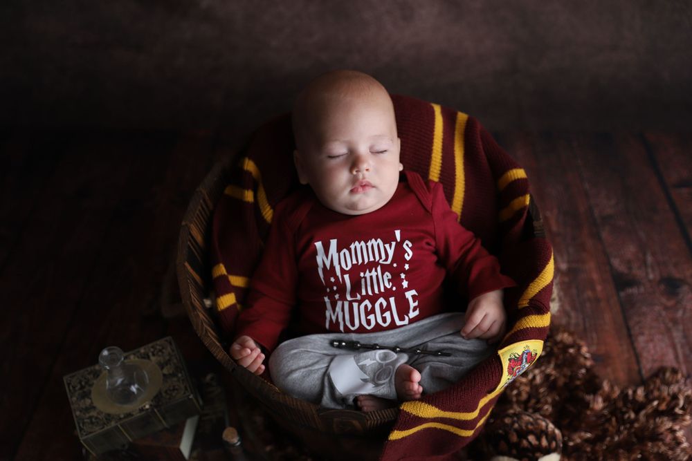 Sleeping newborn in Mommy's Little Muggle Harry Potter outfit rests in wooden basket.