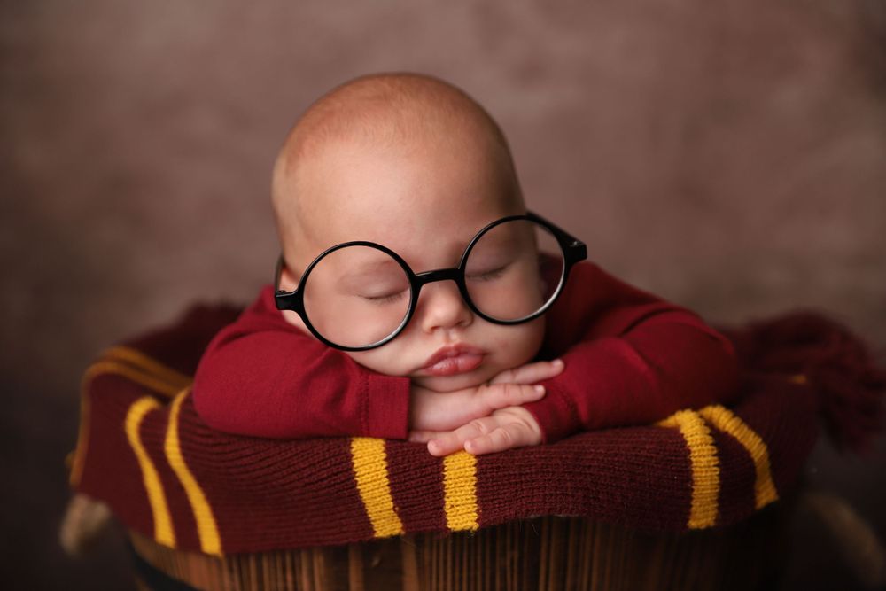 Sleeping newborn wearing oversized round glasses posed in Harry Potter Gryffindor themed basket.