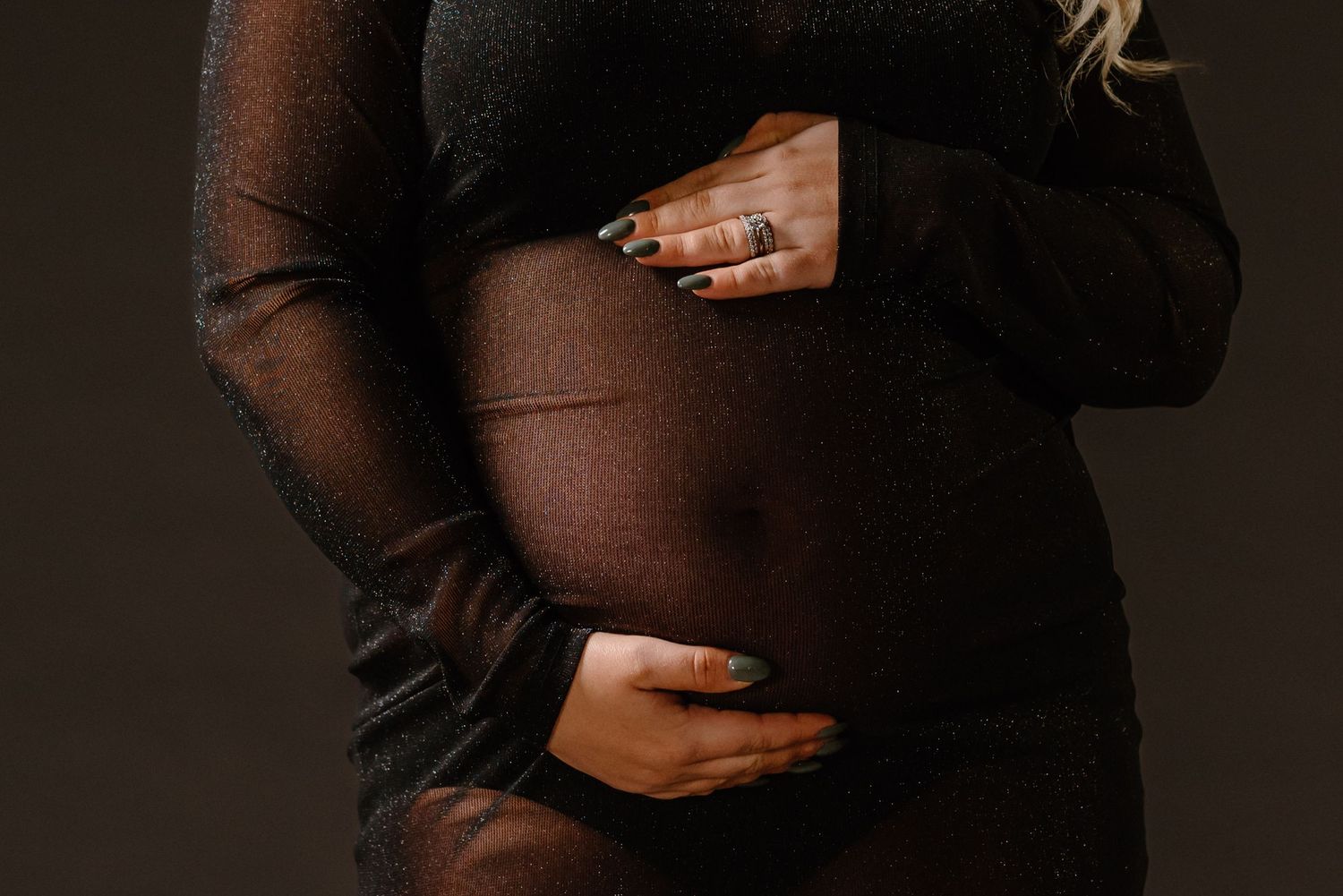 Close-up of hands cradling a pregnant belly in a black sheer dress.