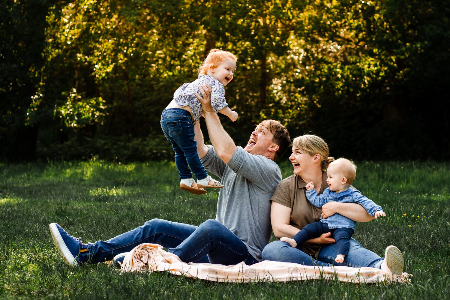 In the forest of Bere, Hampshire, a family of 4 sit surrounded by trees laughing.