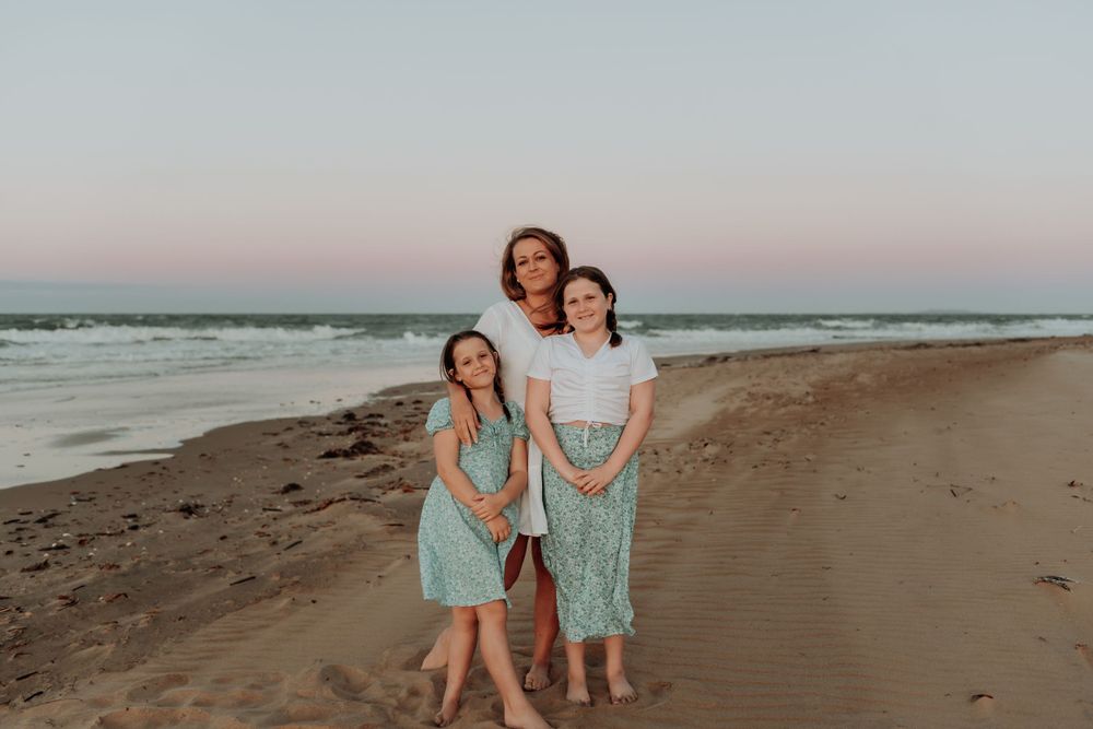 Two people in matching mint green dresses pose together on a sandy gladstone beach at sunset.