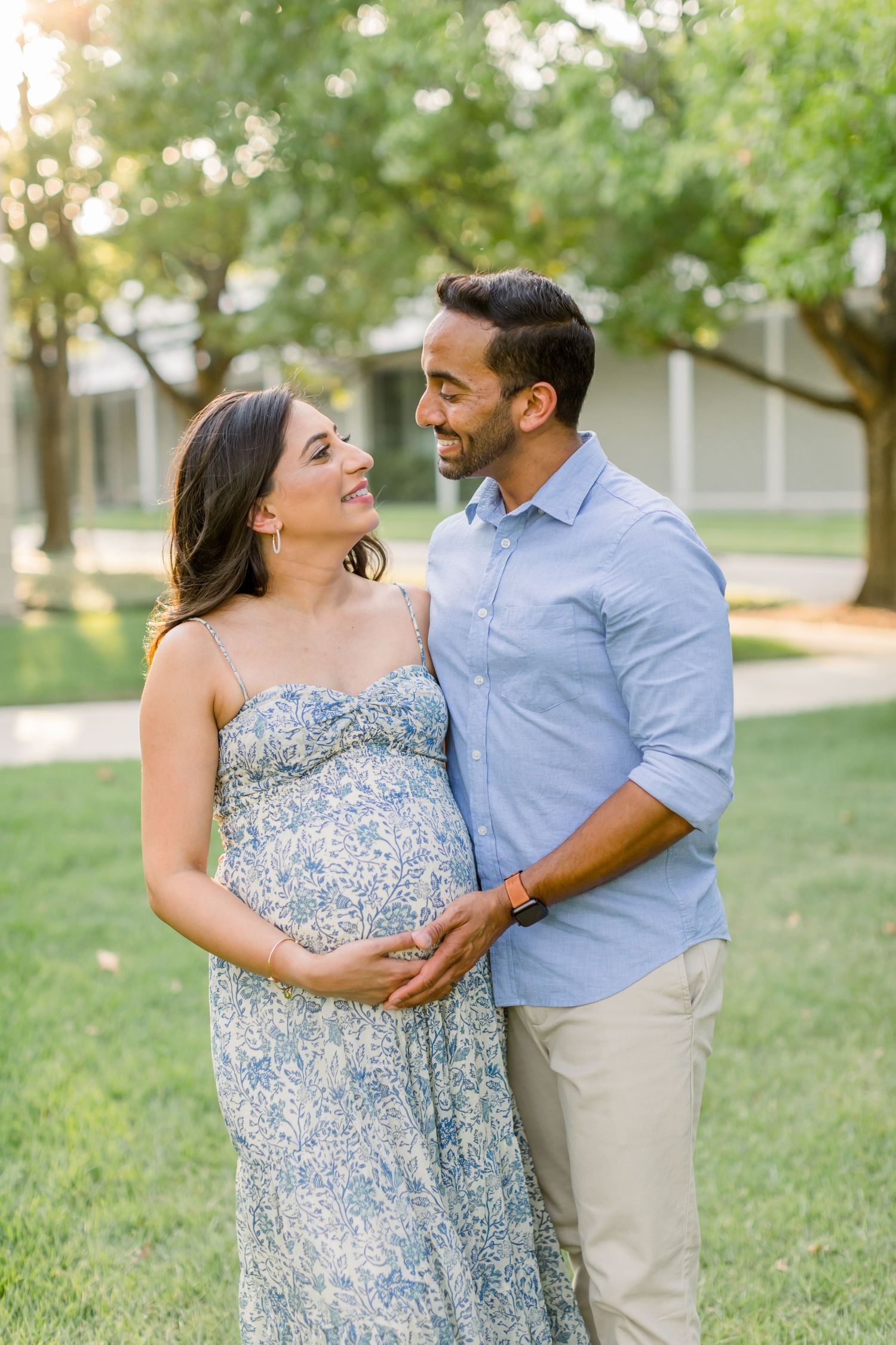 Joyful couple shares loving glance while cradling baby bump outdoors.